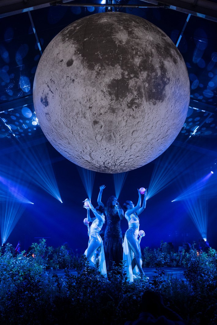 La luna sospesa sopra il palco, con una performance in corso sotto le luci