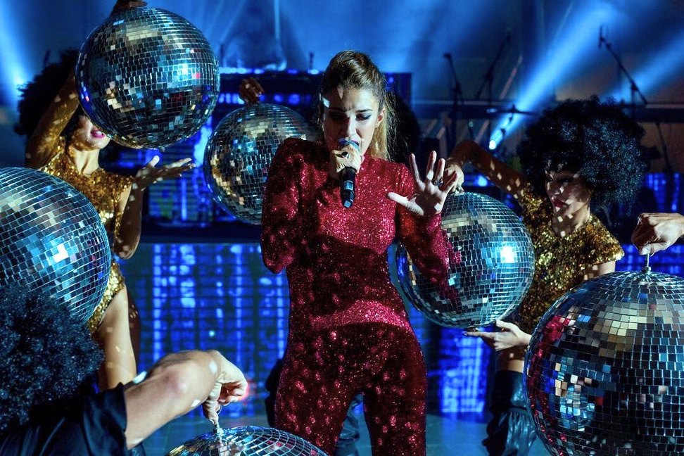 Numero disco con una cantante in tuta di paillettes tra grandi sfere a specchio
