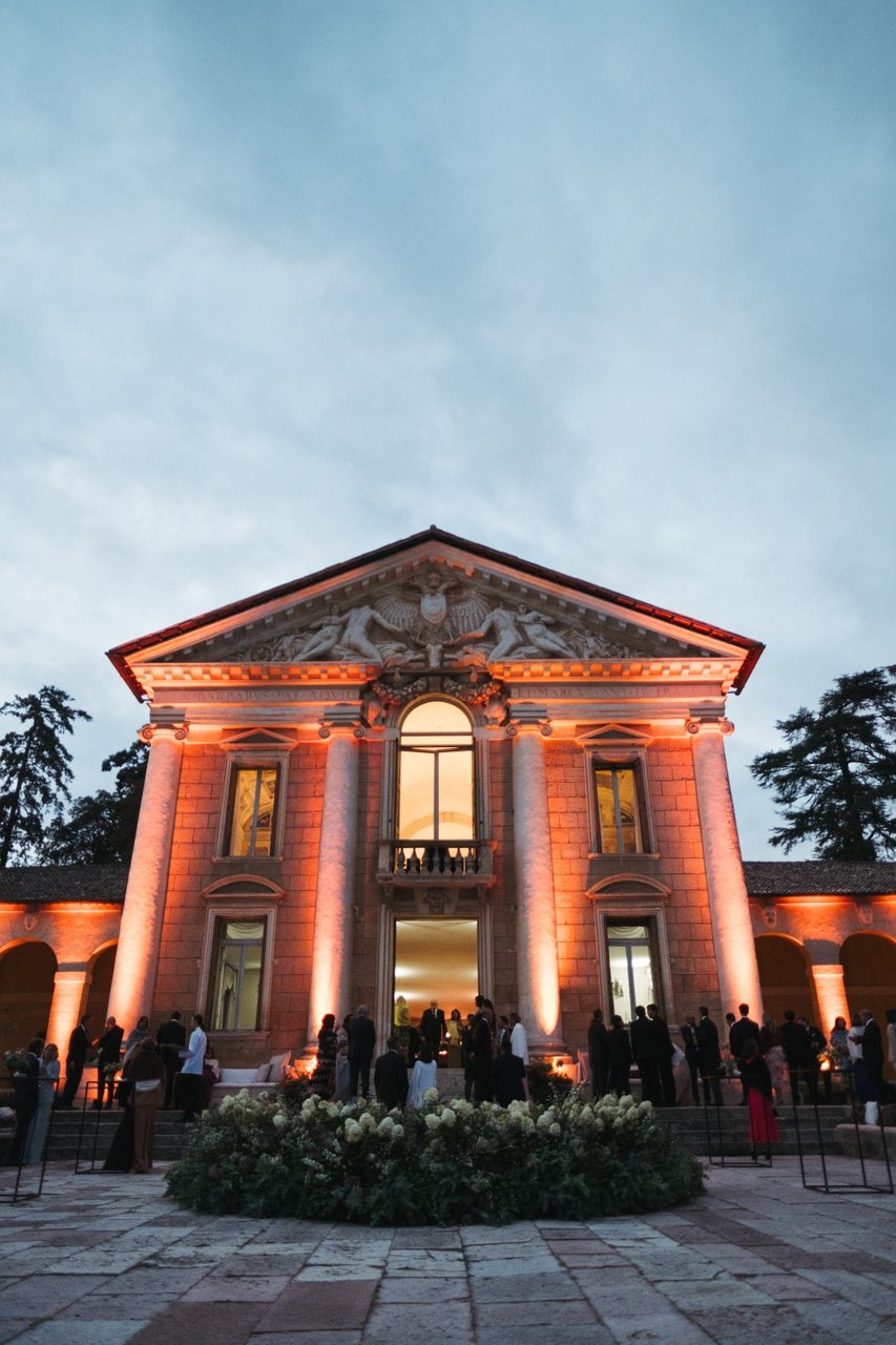 Facciata di una villa palladiana illuminata di ambra al crepuscolo, con il portone aperto sulla luce calda